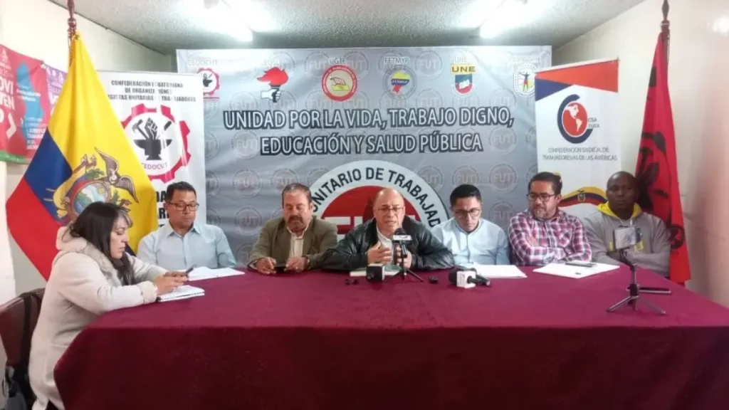 Representantes de sindicatos em reunião na Equador, com bandeiras e pano de fundo referente à luta por direitos trabalhistas.