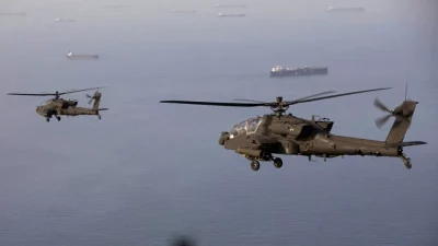 Helicópteros militares voam sobre o mar com navios ao fundo, próximo à região do Estreito de Hormuz. (Foto: aljazeera.com)