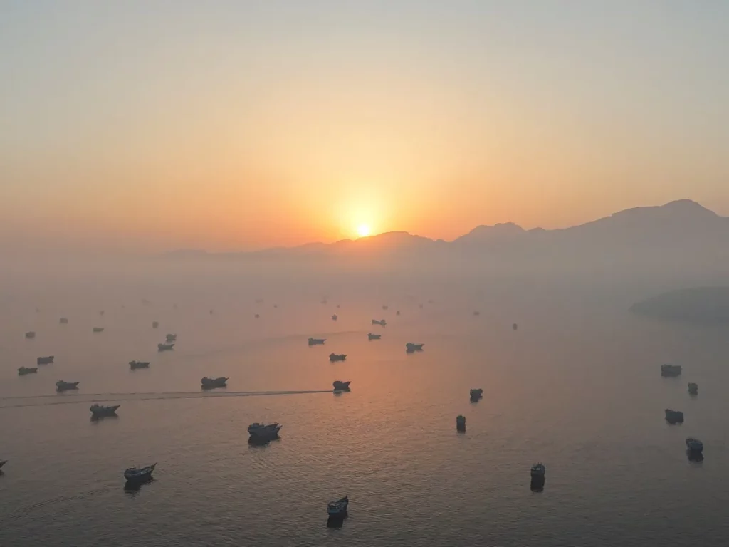 Várias embarcações navegam pela baía durante o amanhecer, com montanhas ao fundo. (Foto: aljazeera.com)