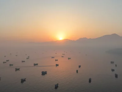 Várias embarcações navegam pela baía durante o amanhecer, com montanhas ao fundo. (Foto: aljazeera.com)