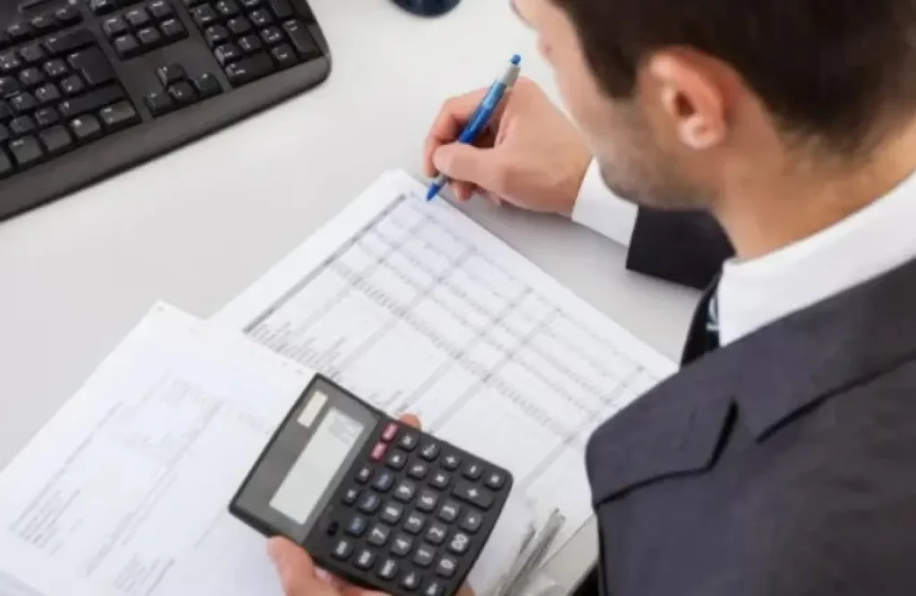 Homem em escritório analisa documentos com calculadora e caneta. (Foto: metropoles.com)