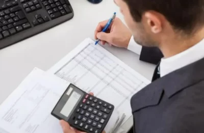 Homem em escritório analisa documentos com calculadora e caneta. (Foto: metropoles.com)