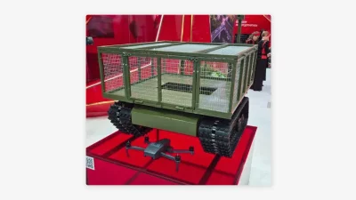 Robô terrestre multifuncional Depesha é exibido em feira militar, com drone ao lado. (Foto: actualidad.rt.com)
