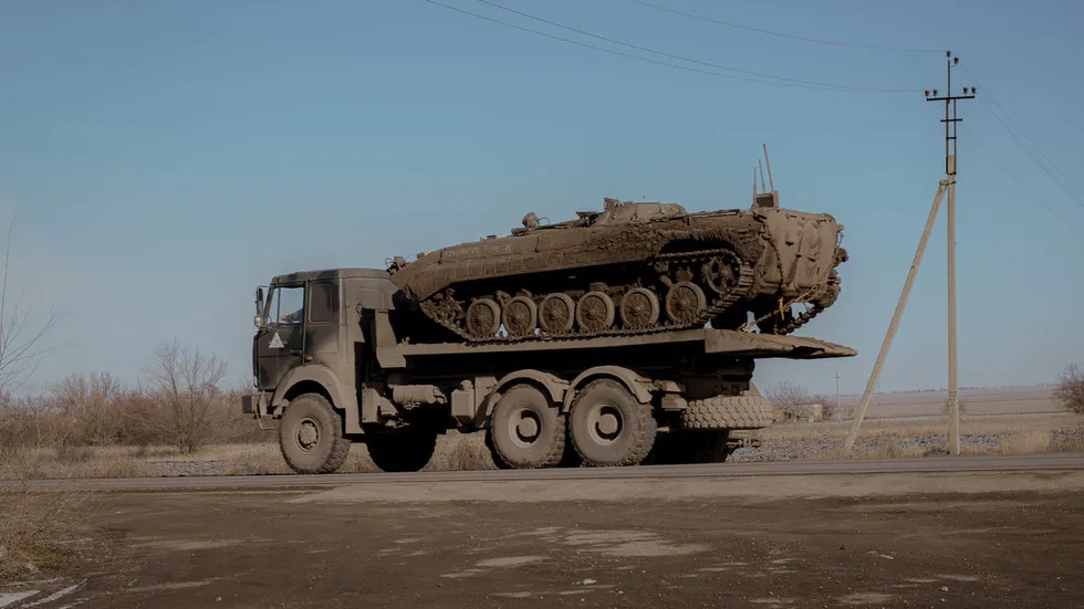 Caminhão transporta um tanque militar em estrada rural. (Foto: rt.com)