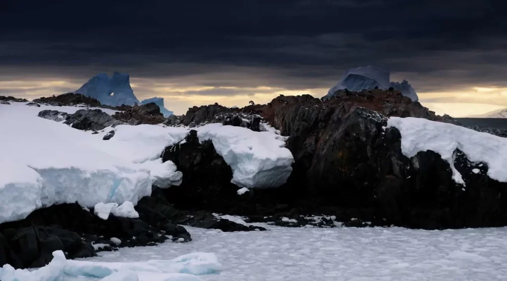 Paisagem antártica com rochas cobertas de neve e gelo sob céu nublado. (Foto: thedebrief.org)