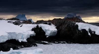 Paisagem antártica com rochas cobertas de neve e gelo sob céu nublado. (Foto: thedebrief.org)