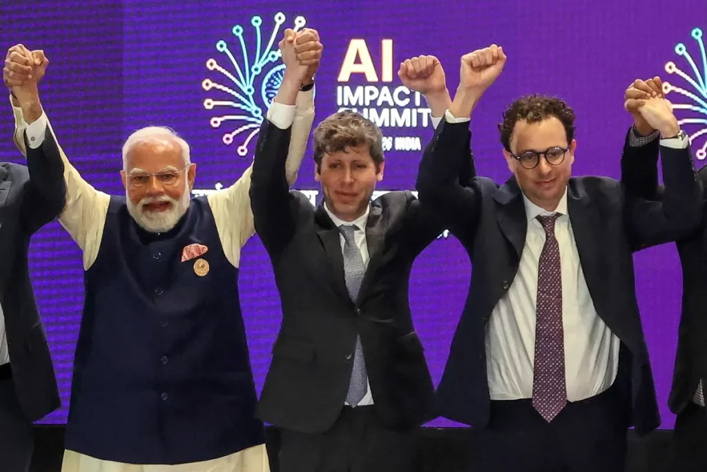 Narendra Modi, Sam Altman e outra figura levantam os punhos em evento do AI Impact Summit. (Foto: techcrunch.com)