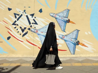 Mulher caminha em frente a mural com representação de aviões militares no Oriente Médio. (Foto: aljazeera.com)