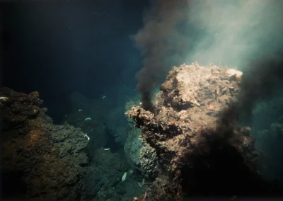 Imagem de ventos hidrotermais no fundo do oceano, com formações rochosas e organismos vivendo em ambiente escuro e quente. (F