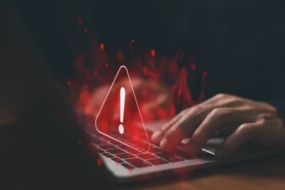 Um usuário digita em laptop com símbolo de alerta e efeitos digitais vermelhos, ilustrando ameaça cibernética. (Foto: olhardi