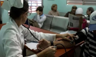 Médica atende paciente em clínica pública, enquanto outros aguardam no fundo. (Foto: ultimasnoticias.com.ve)