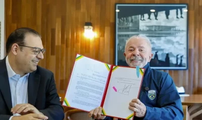 O ex-presidente Lula assina documento ao lado de um homem em ambiente formal. (Foto: cartacapital.com.br)