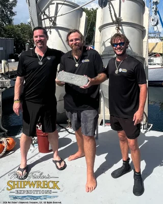 Três membros da equipe Mel Fisher's Shipwreck Expeditions exibem uma barra de prata recuperada do naufrágio do Atocha, em Key