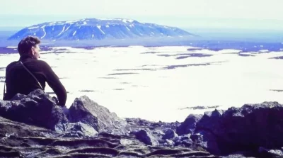 Um homem observa paisagem nevada com montanha ao fundo em região geotérmica. (Foto: cleantechnica.com)