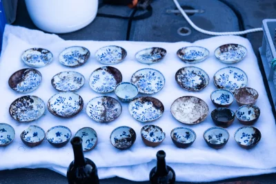 Várias peças de porcelana chinesa com desenhos azuis e brancos são exibidas sobre tecido branco, possivelmente após recuperaç
