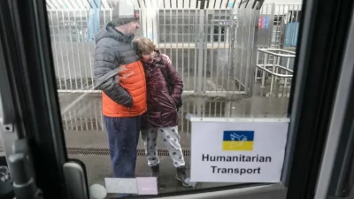 Um casal de refugiados ucranianos aguarda transporte humanitário em local externo. (Foto: rt.com)