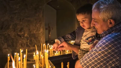 Um homem e uma criança acendem velas em um local de culto. (Foto: actualidad.rt.com)