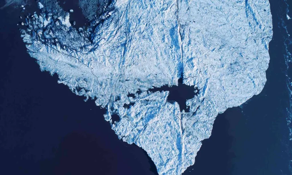 Vista aérea de gelo marinho no Ártico, com formações de icebergs e água escura ao redor. (Foto: earth.com)