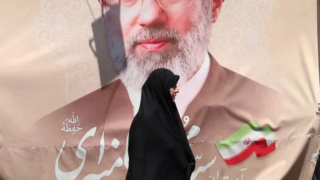 Mulher passa em frente a cartaz com imagem do presidente iraniano Raisi, em Teerã. (Foto: aljazeera.com)