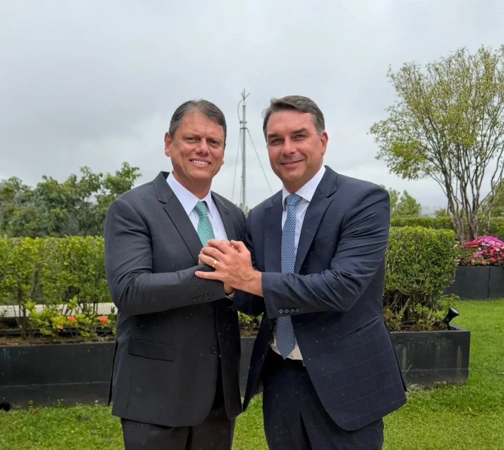Dois homens em traje formal se cumprimentam com um aperto de mão no exterior de um edifício. (Foto: cartacapital.com.br)